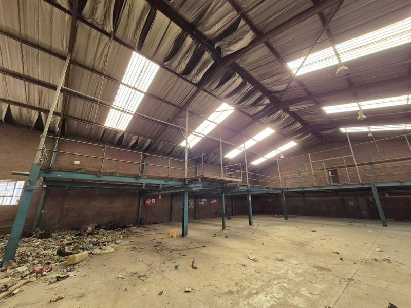 Large industrial utility space featuring exposed brick walls, a steel mezzanine level, and high-pitched metal roofing with integrated skylights.