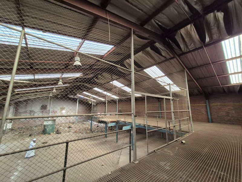Large industrial utility space featuring a steel mezzanine level, metal mesh partitioning, and high-pitched roof with integrated skylights, requiring significant renovation.