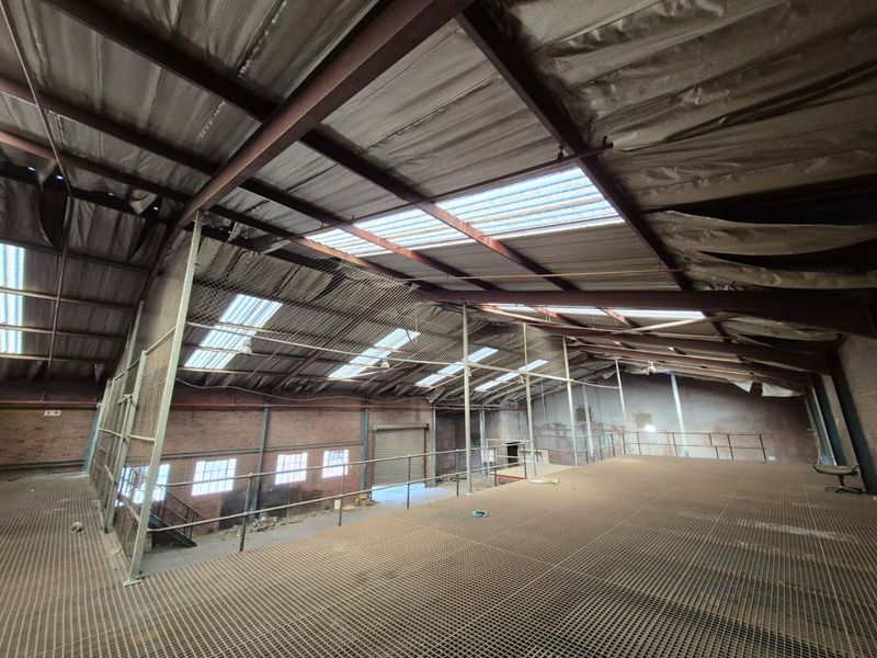 Large industrial utility space featuring a steel mezzanine level, exposed roof trusses, and natural light through integrated skylights.