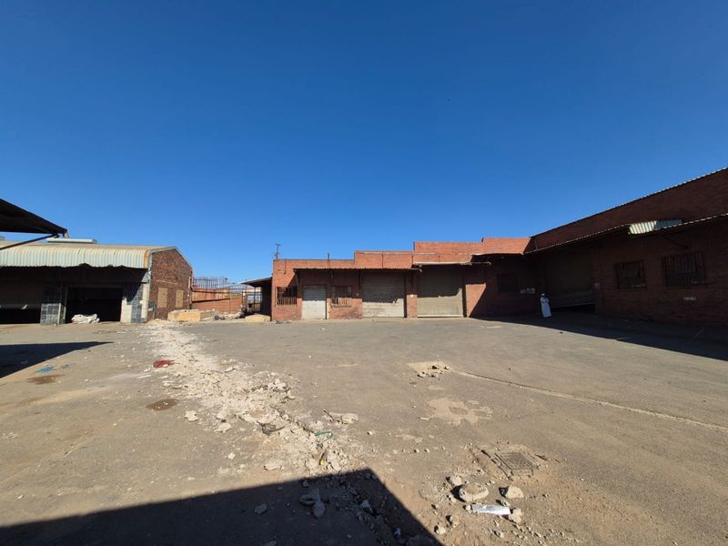 A large industrial-style rear yard featuring brick buildings with multiple roller shutter doors and a worn asphalt surface.