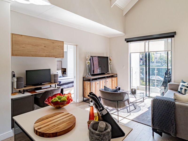 Bright open-plan living area featuring vaulted ceilings, laminate flooring, and direct access to a private balcony, creating a spacious and airy atmosphere.