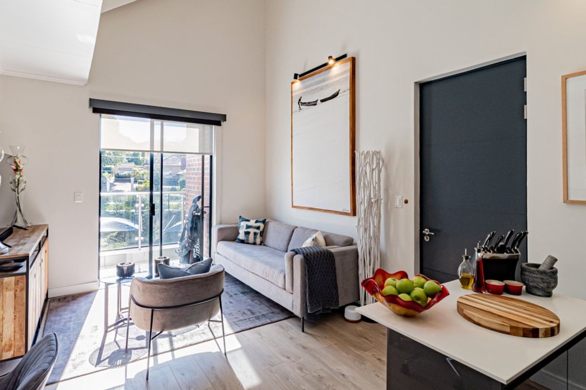 Bright open-plan living area featuring vaulted ceilings, modern laminate flooring, and direct access to a private balcony through sliding glass doors.