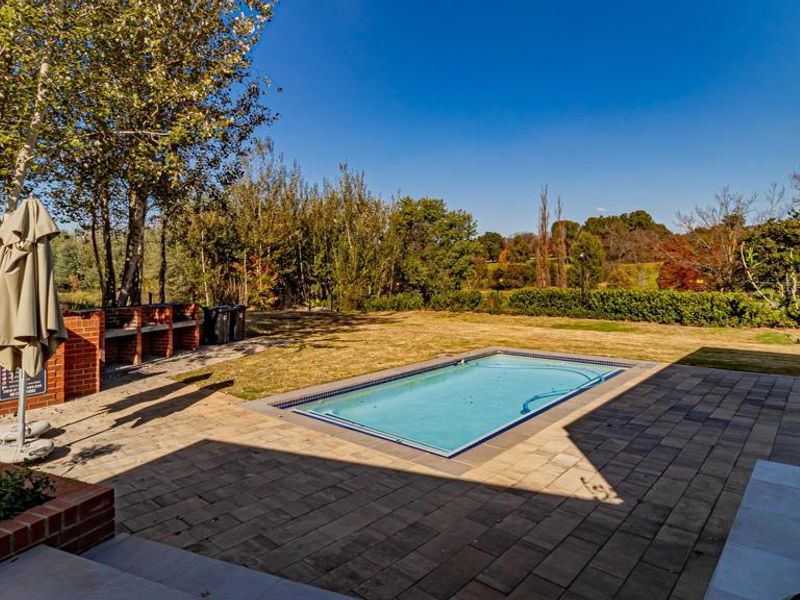 Outdoor pool area featuring a paved patio, built-in brick barbecue, and a swimming pool set within a landscaped garden.