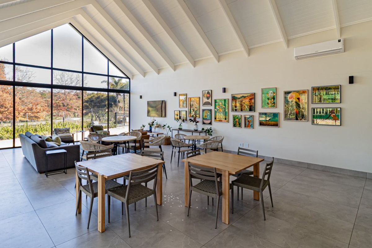Spacious open-plan living area featuring high vaulted ceilings with exposed rafters, large floor-to-ceiling windows, and modern tiled flooring.