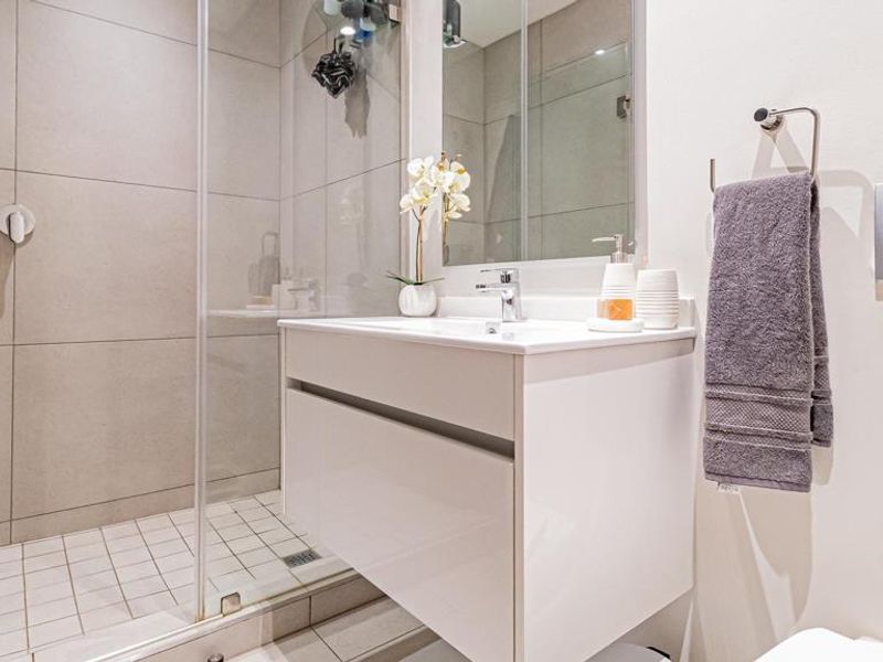 Modern bathroom featuring a wall-mounted vanity, glass-enclosed shower with tiled finishes, and contemporary fixtures.