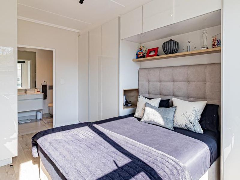 Modern bedroom featuring extensive built-in white cabinetry, overhead storage, and an integrated upholstered headboard, with direct access to an en-suite bathroom.