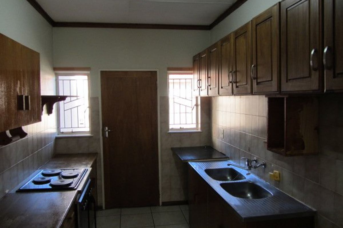A functional kitchen featuring built-in wooden cabinetry, a double stainless steel sink, and an electric hob with tiled splashbacks and flooring.