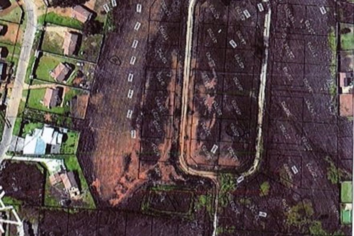 An aerial view of a residential land development showing subdivided plots, internal road infrastructure, and surrounding neighborhood context.