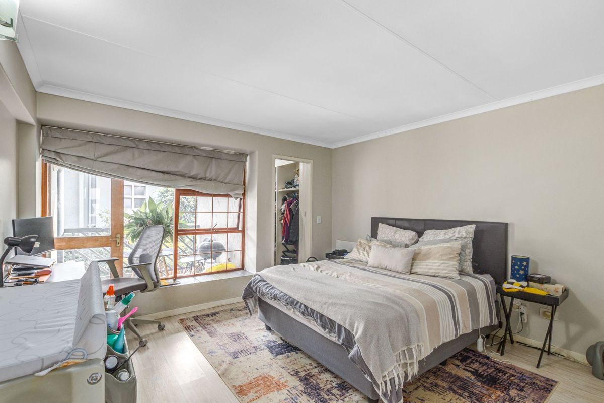 A well-lit bedroom featuring laminate flooring, a built-in closet, and a large window with access to an outdoor area.