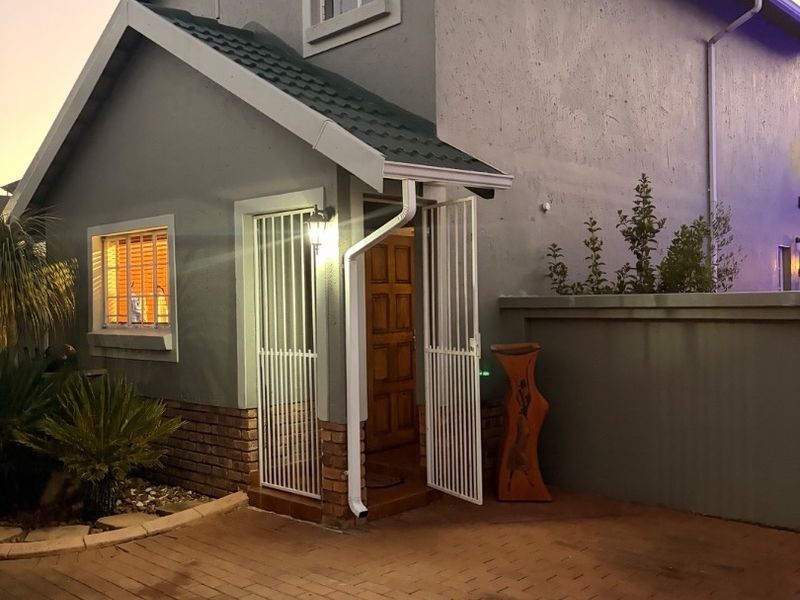 A view of the front entrance featuring a paved driveway, security gate, and exterior lighting at dusk.