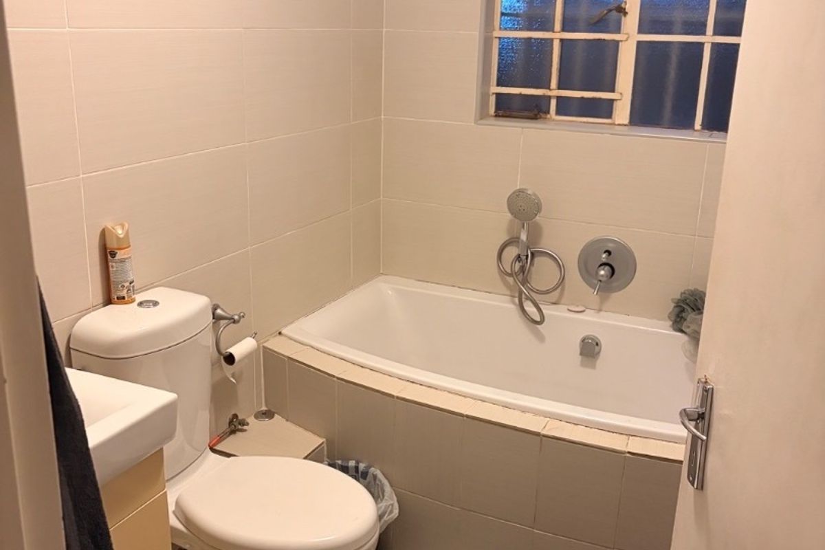 A functional bathroom featuring a built-in bathtub with handheld shower, toilet, and vanity basin, finished with neutral wall and floor tiles.