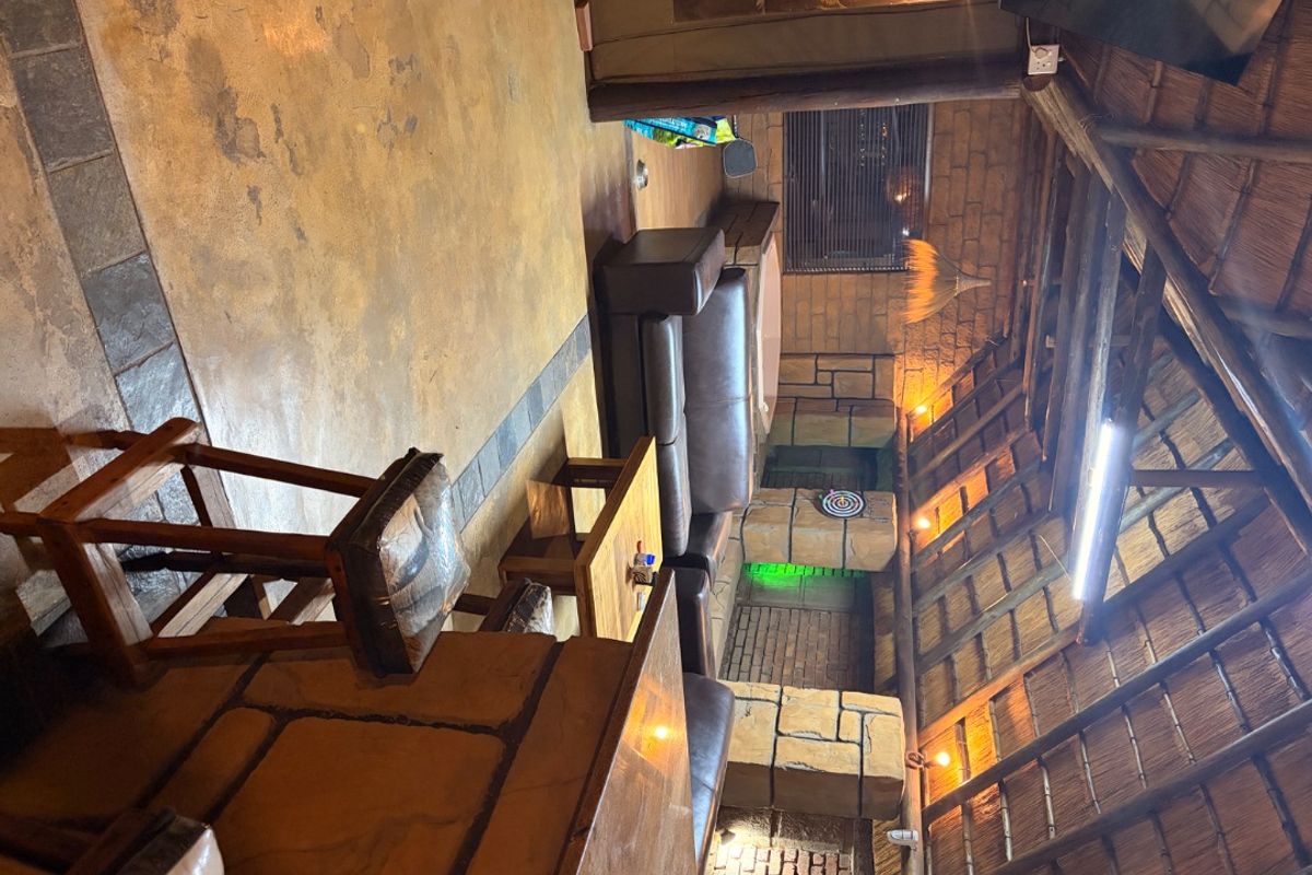 Rustic living area featuring a traditional thatched roof with exposed timber rafters, stone-clad walls, and concrete flooring.