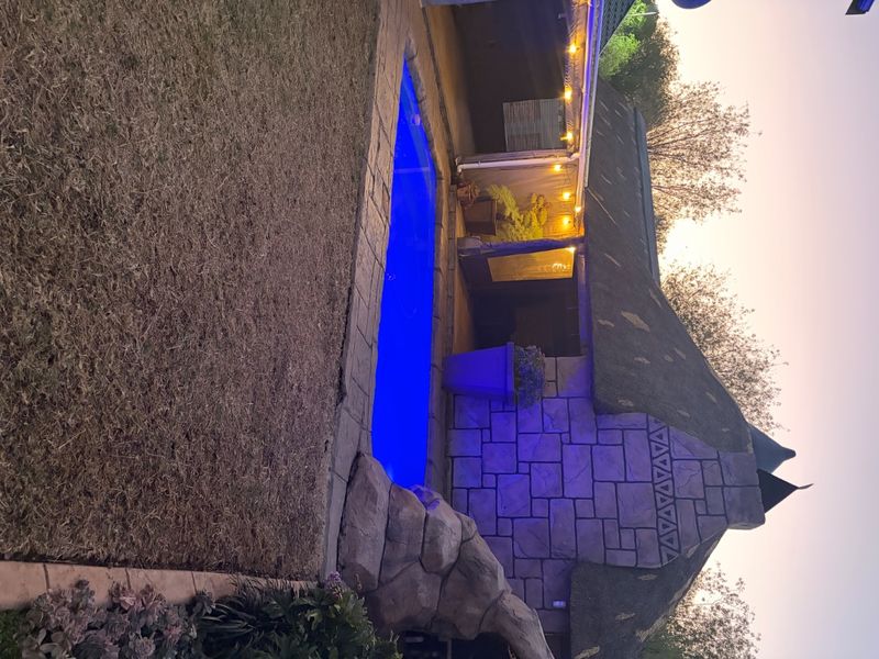 Outdoor pool area featuring a swimming pool, stone-clad wall, and a traditional thatched roof structure, perfect for evening relaxation.