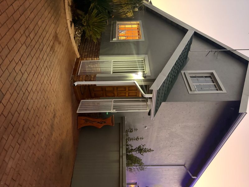 Front entrance view of the house featuring a brick paved driveway, secure gated entry, and a timber front door under a tiled roof.