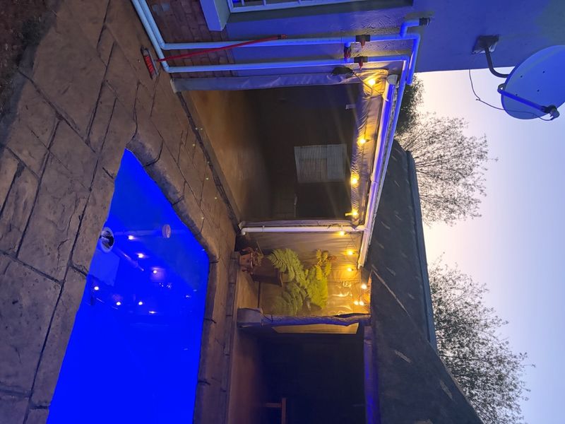 Outdoor pool area featuring a paved deck and a covered patio space with integrated lighting, suitable for evening relaxation.