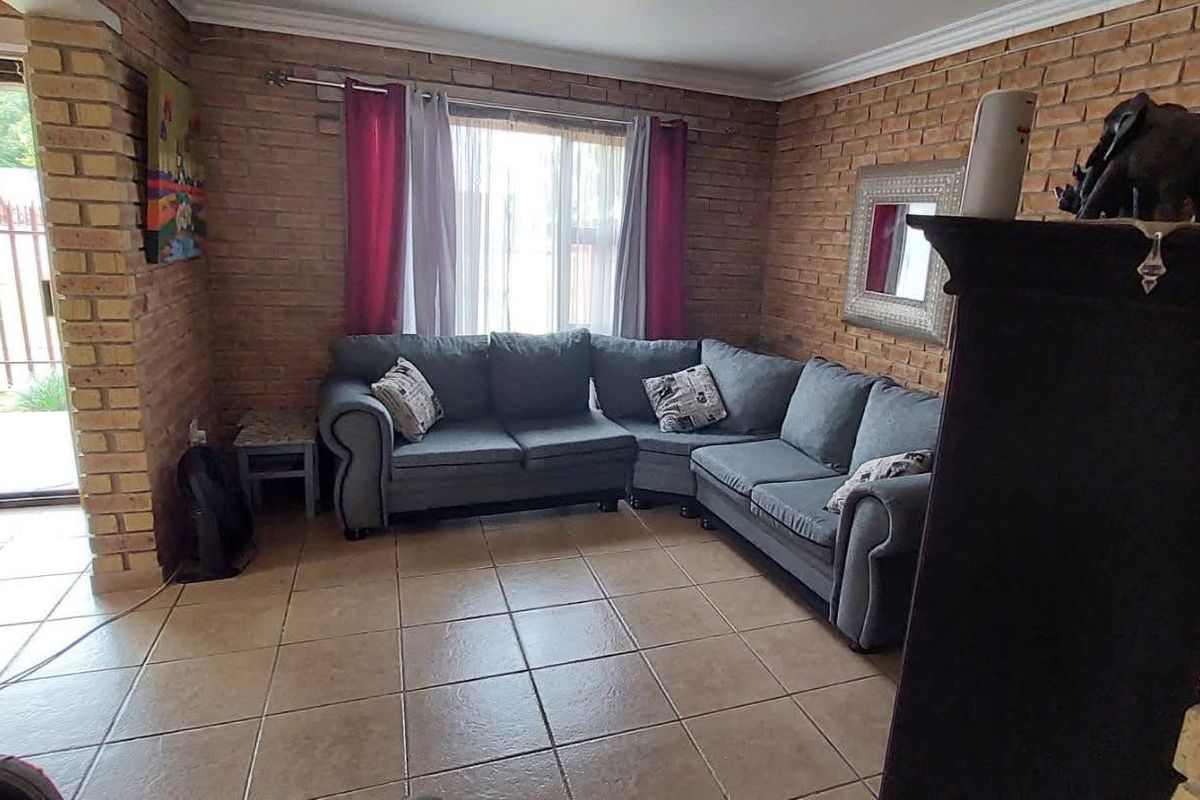 A living room featuring exposed brick walls, tiled flooring, and a sliding glass door providing access to the outdoor area.