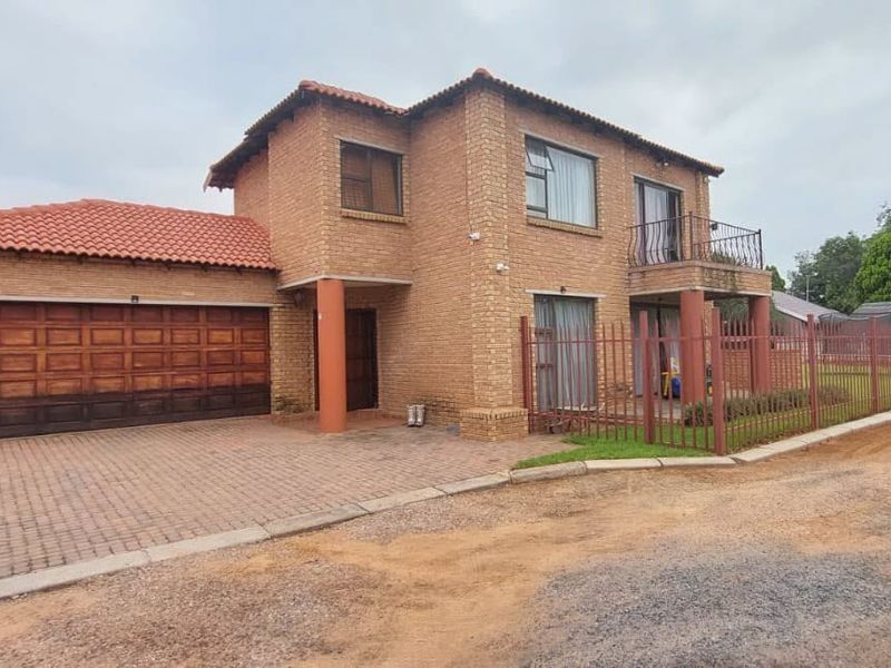 A double-story face brick house featuring a tiled roof, double garage, and a balcony, secured by perimeter metal fencing.