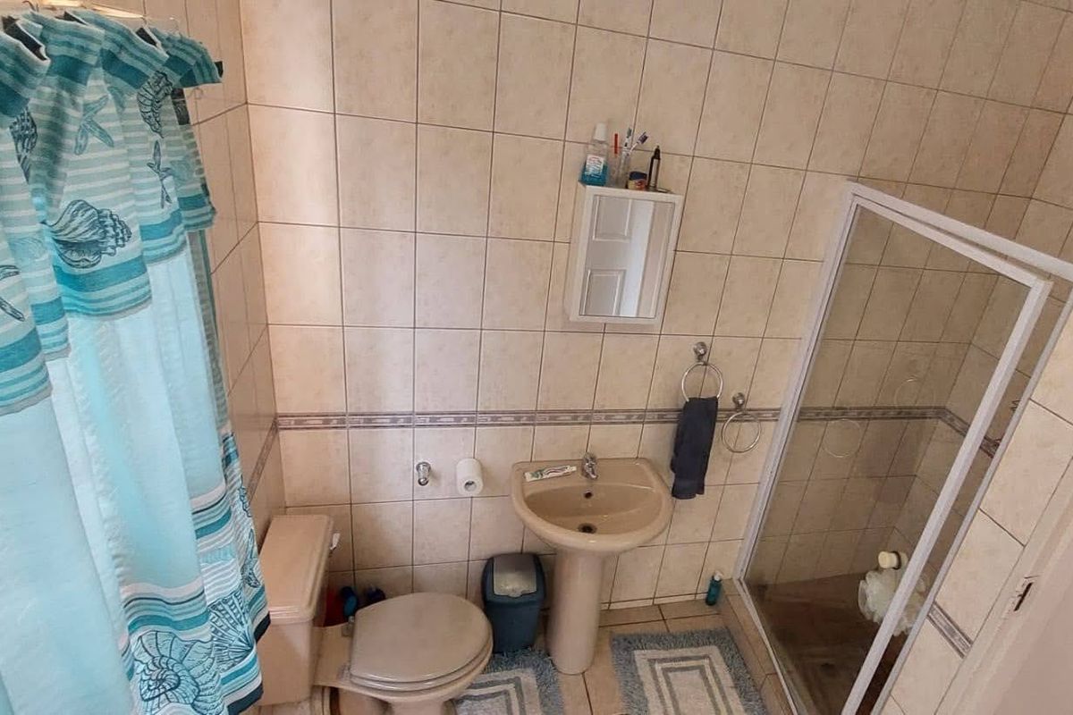 A functional bathroom featuring a pedestal basin, toilet, and a glass-enclosed shower with neutral wall tiling.