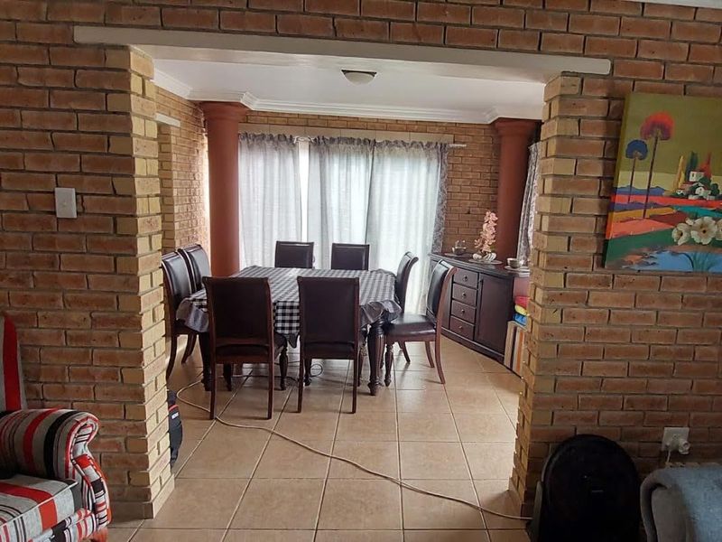 Open plan living and dining area featuring exposed brick walls, ceramic floor tiles, and decorative columns leading to a bright patio space.