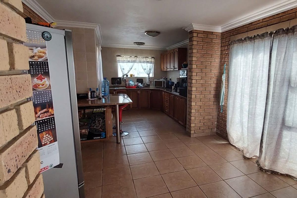 A functional kitchen featuring wooden cabinetry, tiled flooring, and an exposed brick pillar, offering a practical layout with a breakfast counter.