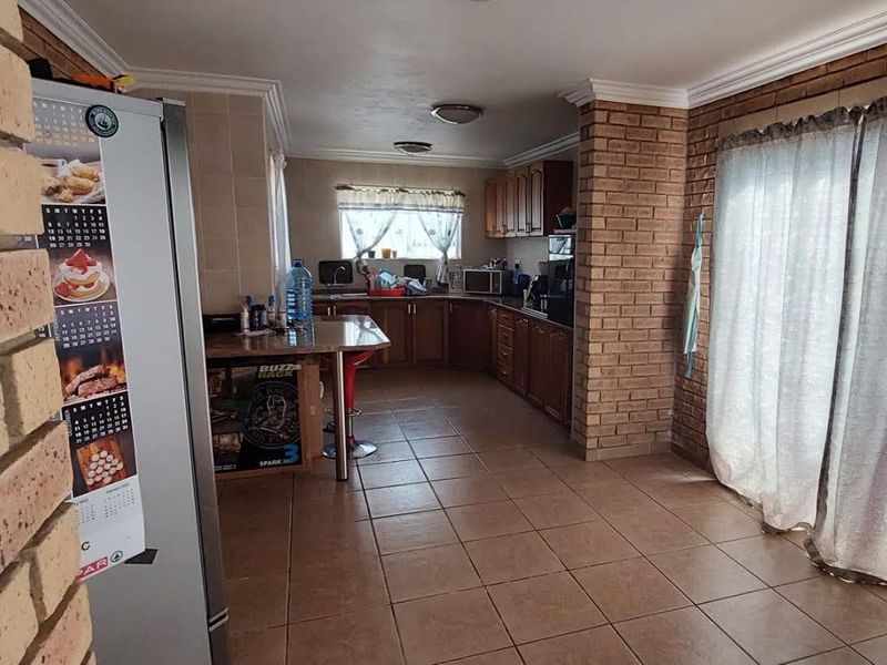 A functional kitchen featuring wooden cabinetry, tiled flooring, and an exposed brick pillar, offering a practical layout with a breakfast counter.