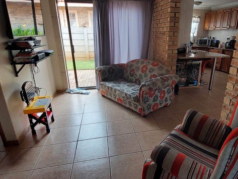 Open-plan living area featuring ceramic floor tiles, an exposed brick feature wall, and a functional kitchen with a breakfast bar and sliding door access.