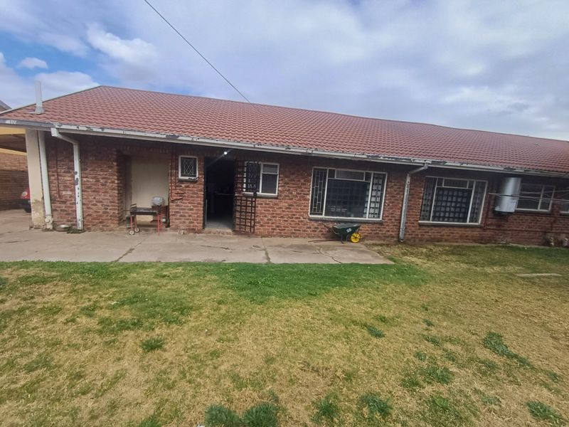 Rear view of a single-story brick house featuring a tiled roof, concrete patio area, and security-fitted windows.