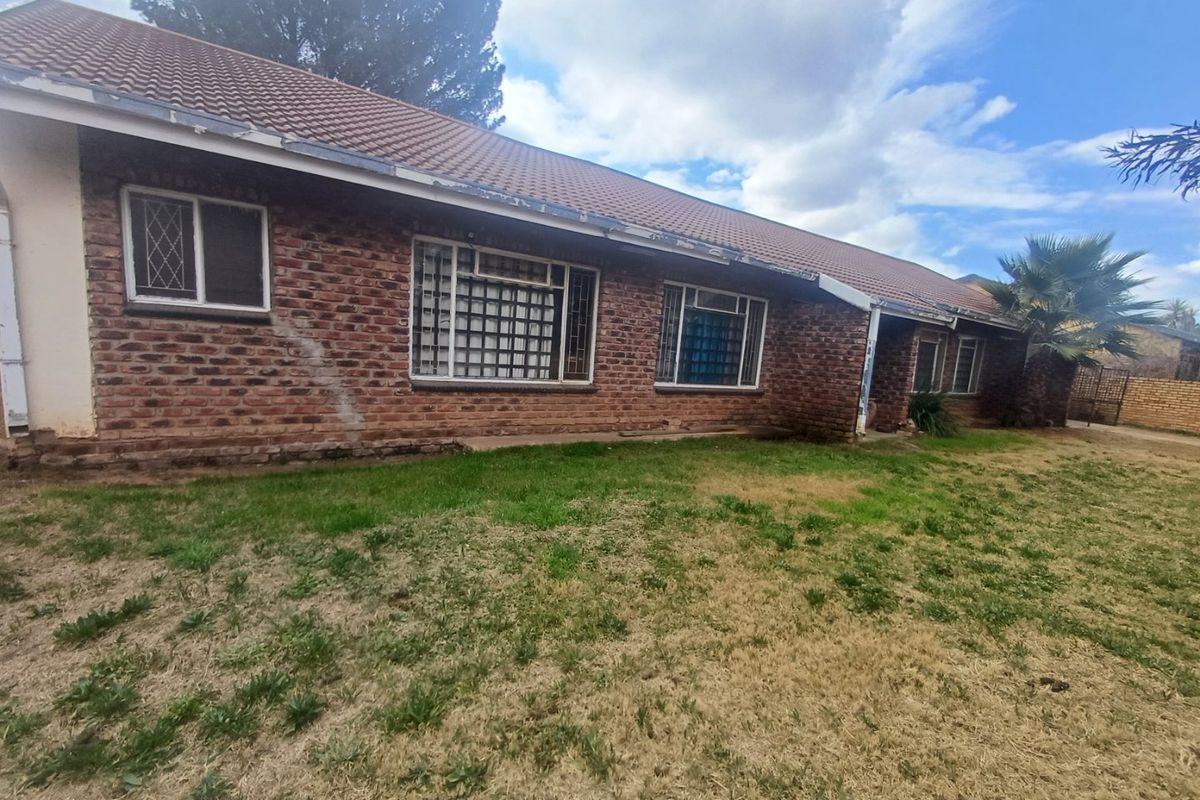 Rear view of a single-story brick house featuring a tiled roof and security-barred windows, set against a large lawn area.