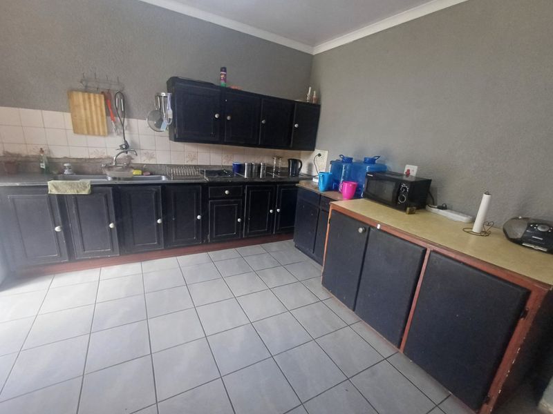 A functional kitchen featuring dark built-in cabinetry, a stainless steel sink, tiled backsplash, and neutral floor tiles.