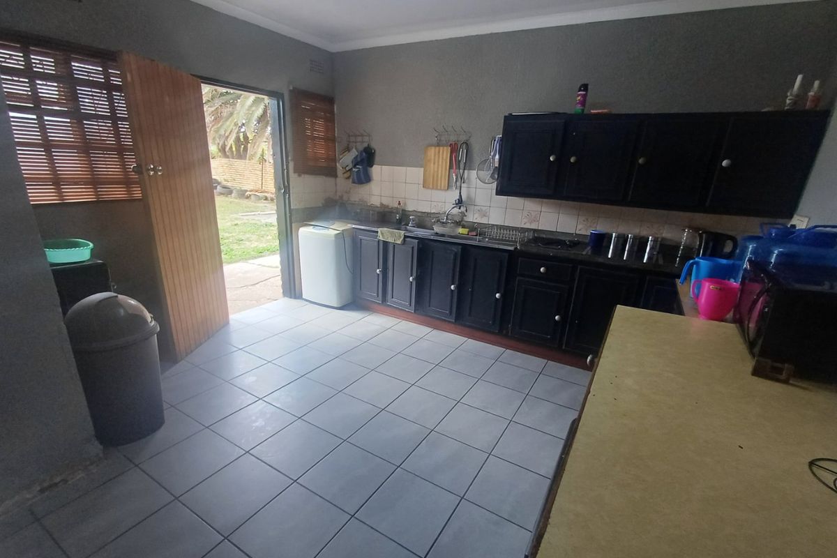 A functional kitchen featuring dark built-in cabinetry, tiled flooring, and direct access to the rear garden area.