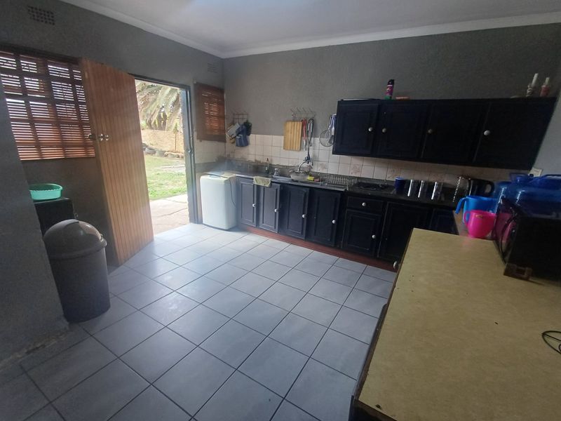 A functional kitchen featuring dark built-in cabinetry, tiled flooring, and direct access to the rear garden area.