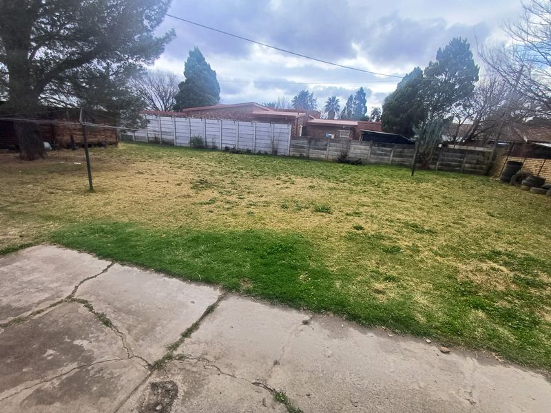 A spacious rear garden featuring a concrete patio area, a large lawn, and secure precast concrete boundary walling.