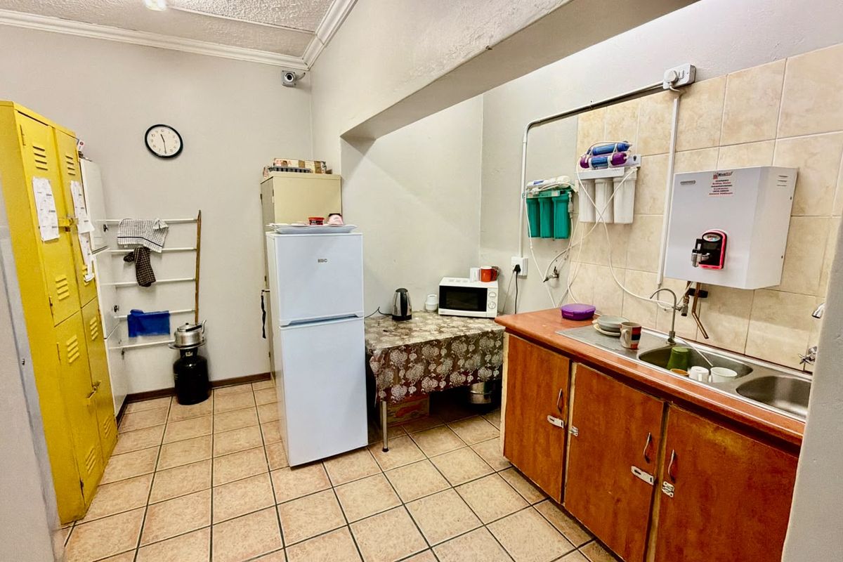 A functional commercial kitchen area featuring tiled flooring, built-in cabinetry, a double basin sink, and a wall-mounted water filtration and heating system.