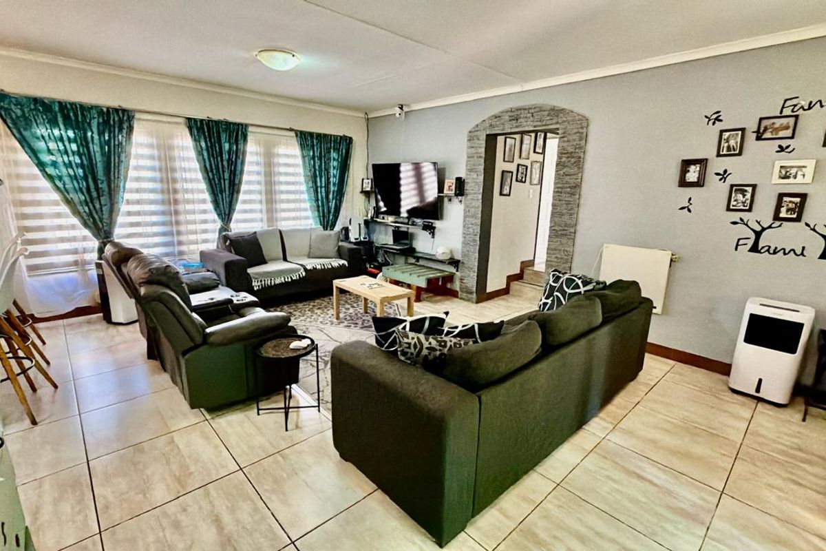 Spacious living room featuring tiled flooring, a distinctive stone-clad arched doorway, and large windows with fitted blinds, offering a comfortable and functional layout.