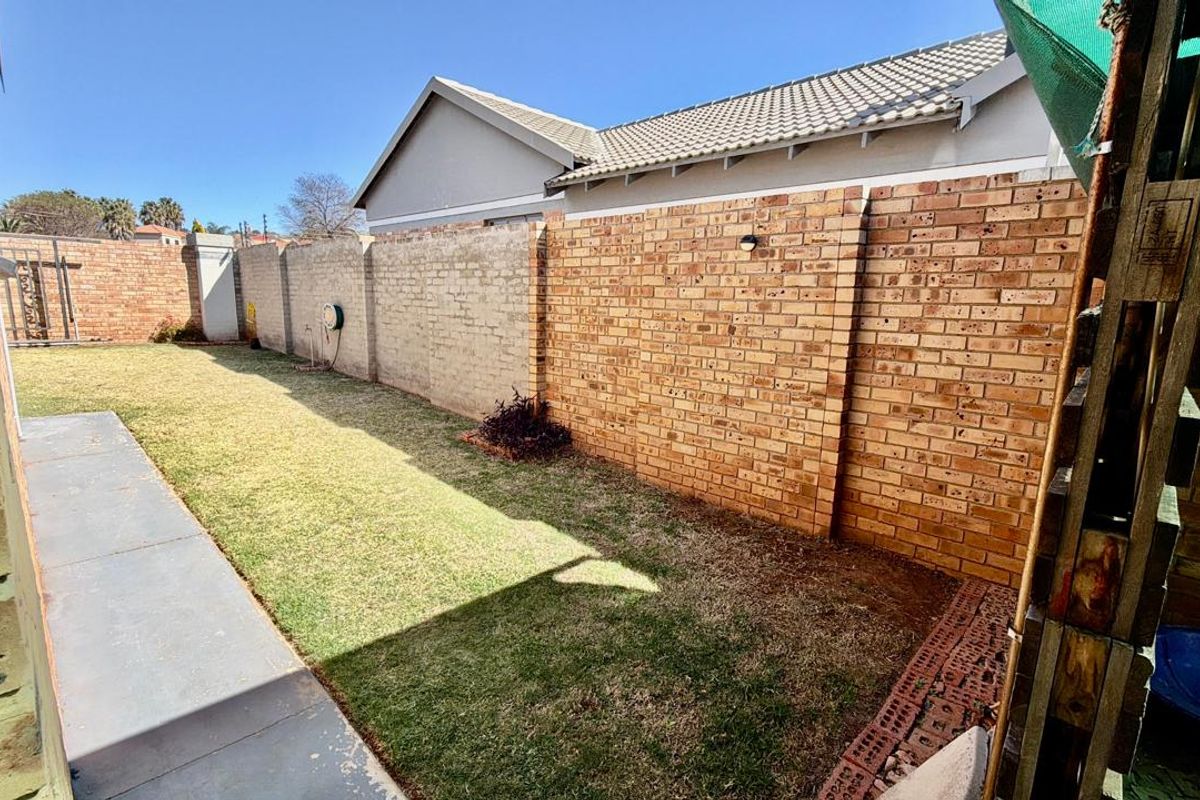 A private rear garden featuring a lawn, concrete pathway, and high brick boundary walls, offering a blank canvas for outdoor landscaping.