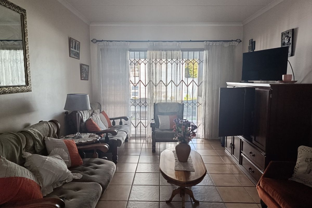 A comfortable living room featuring tiled flooring, coved ceilings, and a sliding glass door with a security gate leading to an outdoor area.
