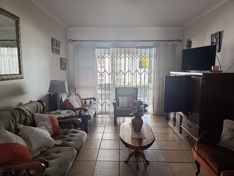 A comfortable living room featuring tiled flooring, coved ceilings, and a sliding glass door with a security gate leading to an outdoor area.