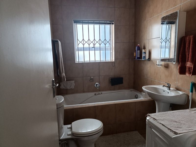 A functional bathroom featuring a bathtub, pedestal basin, toilet, and tiled walls, equipped with a window security gate and a wall-mounted medicine cabinet.