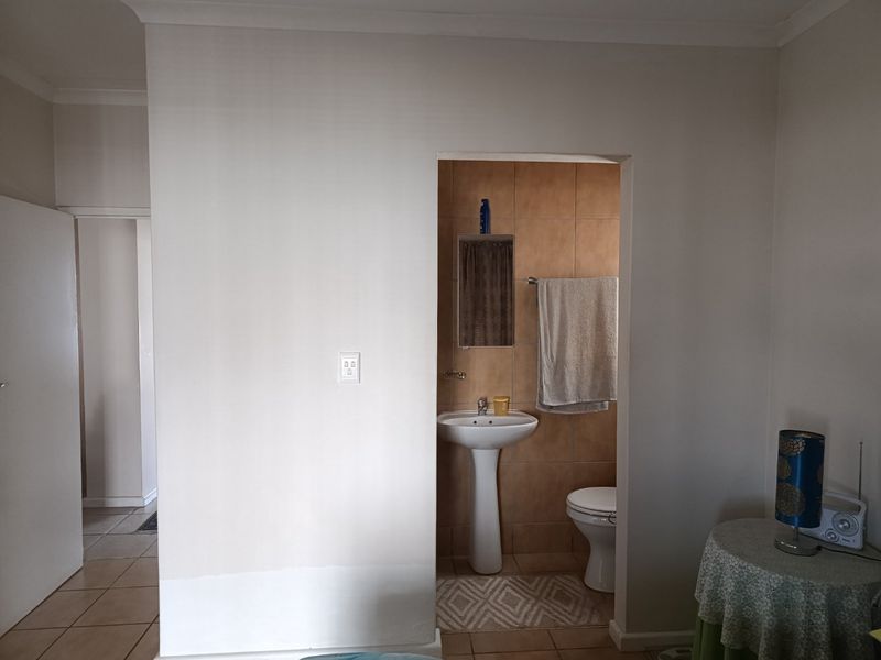 A compact bathroom featuring a pedestal sink, toilet, and neutral wall tiling, accessible from the adjacent living area.