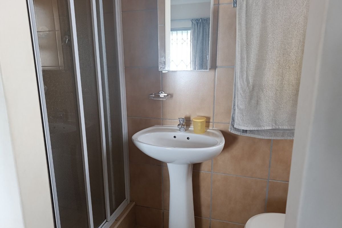 A functional bathroom featuring a pedestal basin, shower enclosure, and neutral wall tiling.