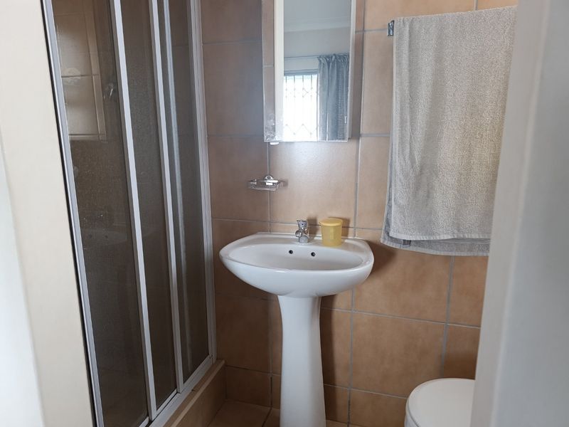 A functional bathroom featuring a pedestal basin, shower enclosure, and neutral wall tiling.