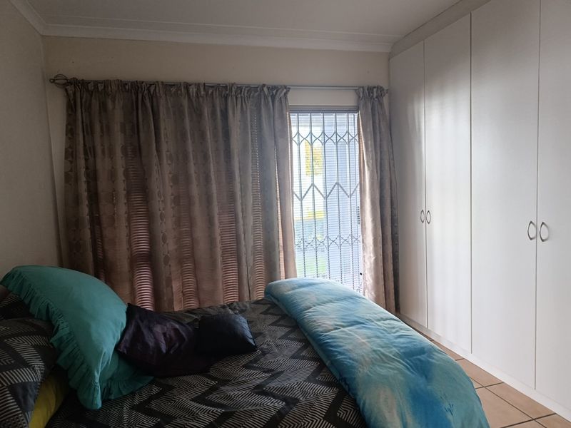 A bedroom featuring built-in cupboards, tiled flooring, and a security gate over the window, providing a functional and secure living space.
