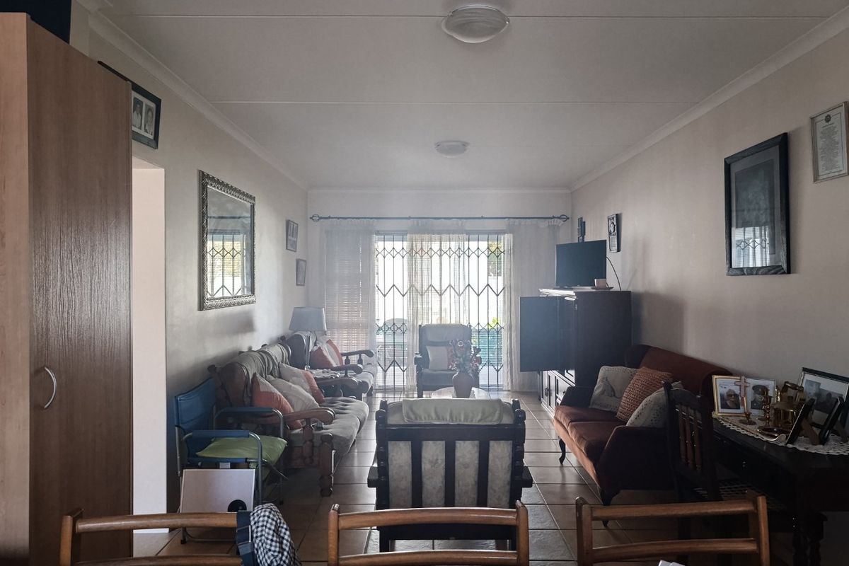A spacious living room featuring tiled flooring and a sliding glass door with security gate, providing access to the outdoor area.