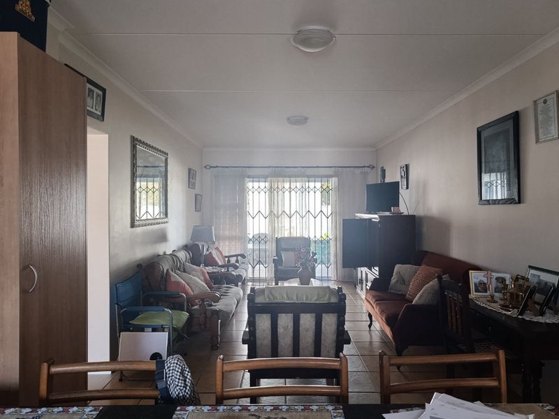 A spacious living room featuring tiled flooring and a sliding glass door with security gate, providing access to the outdoor area.