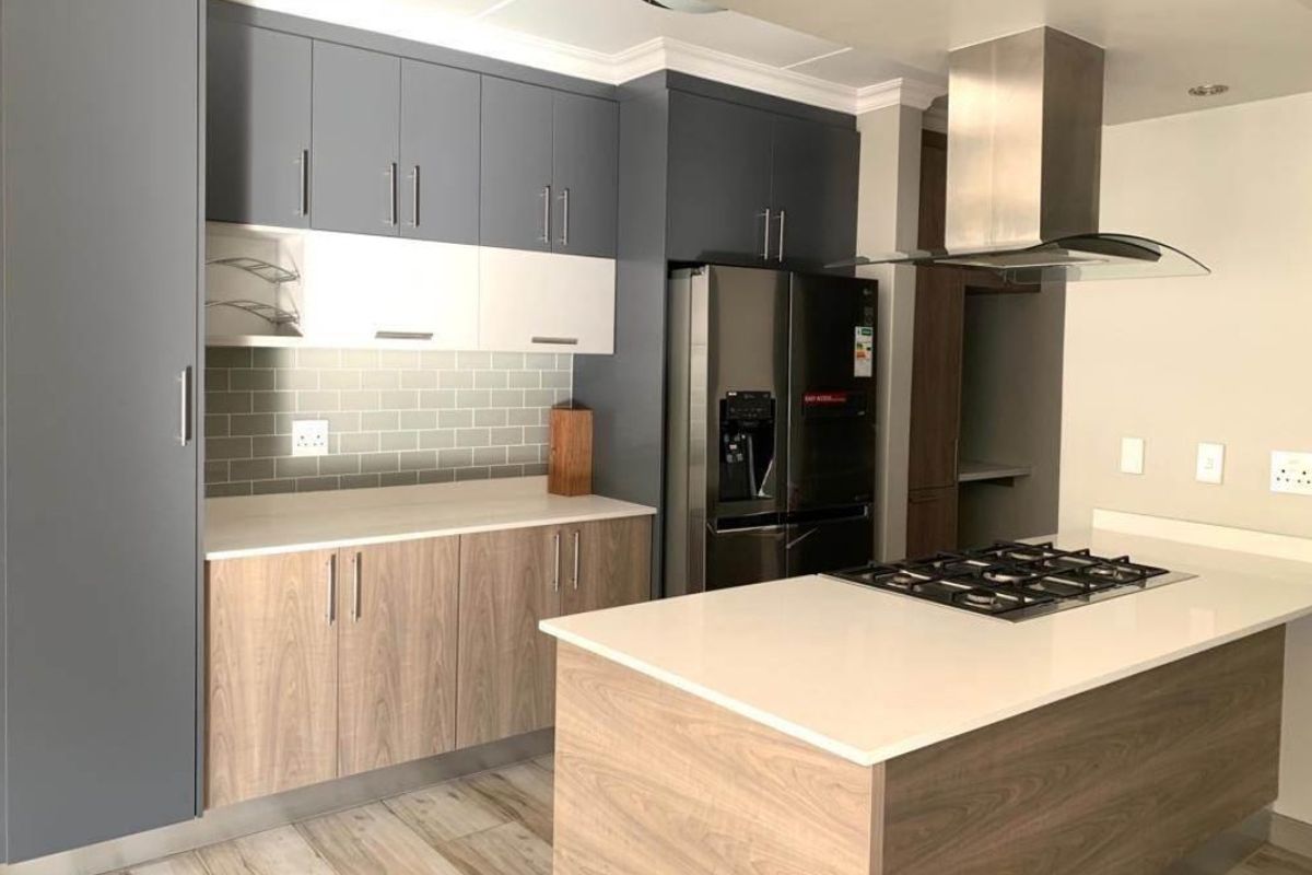 Modern kitchen featuring two-tone cabinetry, stone countertops, a central island with a gas hob, stainless steel extractor fan, and a subway tile backsplash.