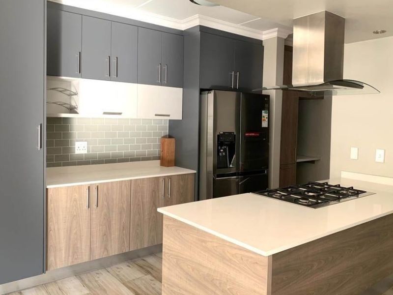 Modern kitchen featuring two-tone cabinetry, stone countertops, a central island with a gas hob, stainless steel extractor fan, and a subway tile backsplash.