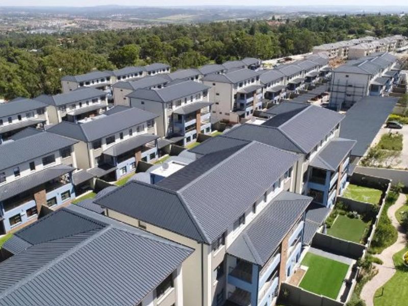 Aerial view of a modern apartment complex featuring multiple residential blocks with pitched roofs, private balconies, and landscaped communal garden areas.