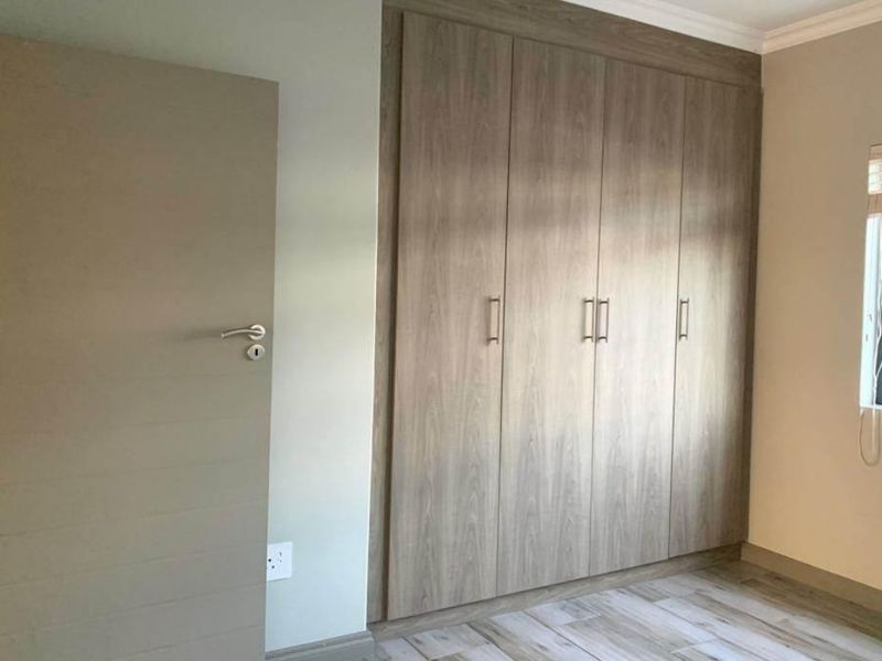 A clean, modern bedroom featuring neutral walls, wood-look laminate flooring, and ample built-in cupboard storage.