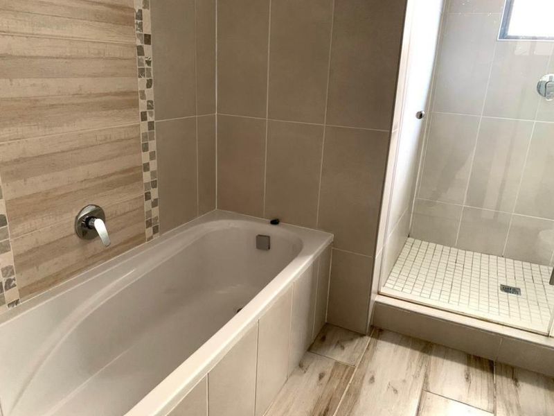 A modern bathroom featuring a built-in bathtub, a separate shower enclosure, and neutral-toned wall and floor tiling.