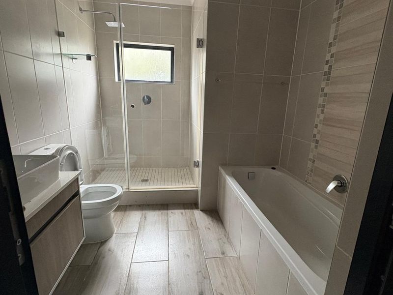 Modern bathroom featuring a walk-in shower with glass screen, a built-in bathtub, vanity cabinet, and neutral tiled finishes throughout.